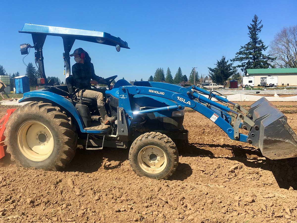 woman driving a TC40 tractor over bare farm soil